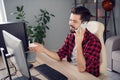 Photo of charming happy young man talk phone sit desk good mood job computer indoors inside office Royalty Free Stock Photo