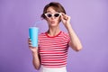 Photo of charming lady hold specs soda plastic takeaway cup send air kiss wear sunglass striped t-shirt isolated purple