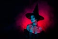 Photo of charming lady magician on theme carnival fest wear witchery costume isolated on fog dark colored background Royalty Free Stock Photo