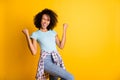 Photo of charming lucky dark skin wavy lady wear blue t-shirt rising fists empty space isolated yellow color background