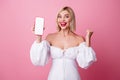 Photo of charming lucky lady wear off shoulders dress rising fist modern gadget display empty space isolated pink color