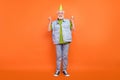 Photo of charming lucky retired man wear vintage jeans waistcoat birthday headwear rising fists smiling isolated orange