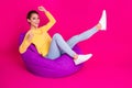 Photo of charming lucky young lady wear yellow jumper smiling sitting bean bag rising fists isolated pink color Royalty Free Stock Photo