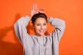 Photo of charming playful young lady wear grey sweatshirt smiling showing arms bunny ears isolated orange color Royalty Free Stock Photo