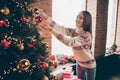 Photo of charming shiny mature woman wear print sweater smiling decorating christmas tree indoors house home room