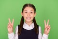 Photo of charming shiny school girl dressed formal clothes smiling showing v-signs green color background