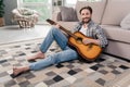 Photo of charming sweet mature guy dressed checkered shirt sitting floor playing guitar indoors apartment room Royalty Free Stock Photo