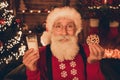 Photo of charming sweet mature man dressed santa costume smiling holding milk glass tasty biscuit indoors home room