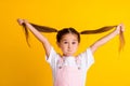 Photo of charming sweet school girl wear summer outfit bloated cheeks holding long tails isolated yellow color