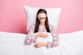 Photo of charming sweet young woman sleepwear mask lying pillow covering duvet isolated pink color background