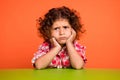 Photo of charming upset schoolgirl wear plaid outfit sitting green table arms cheeks isolated orange color background