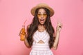 Photo of charming woman 20s wearing sunglasses and straw hat drinking soda from glass bottle, isolated over pink background Royalty Free Stock Photo