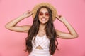 Photo of charming woman 20s wearing sunglasses and straw hat smiling at camera, isolated over pink background
