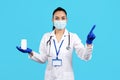 Photo of charming young woman doctor holding bottle of pills and pointing finger away over blue background. Royalty Free Stock Photo