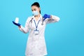 Photo of charming young woman doctor holding bottle of pills and showing bad gesture with hand over blue background. Royalty Free Stock Photo