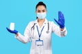 Photo of charming young woman doctor holding bottle of pills and showing stop gesture with hand over blue background. Royalty Free Stock Photo