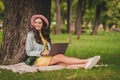 Photo of charming young woman dressed teal jacket glasses bag cap sitting green grass writing modern device outdoors