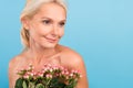Photo of cheerful adorable senior woman nude shoulders holding flowers bouquet looking empty space isolated blue color Royalty Free Stock Photo