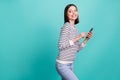 Photo of cheerful curious lady hold cellphone look back wear striped shirt isolated on turquoise color background