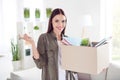 Photo of cheerful cute young woman dressed green shirt holding paper box new apartment keys indoors house home room Royalty Free Stock Photo