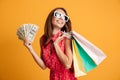 Photo of cheerful elegant young woman in sunglasses and red dress holding fan of money and colorful shopping bags, looking aside Royalty Free Stock Photo