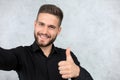 Photo of cheerful handsome young man standing over grey background showing thumbs up