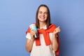 Photo of cheerful joyful young adult woman wearing white T-shirt and orange sweater tied over shoulders standing isolated on blue Royalty Free Stock Photo
