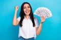 Photo of cheerful lucky girl dressed white shirt rising fist holding cash fan isolated blue color background Royalty Free Stock Photo