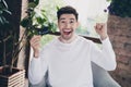 Photo of cheerful lucky young guy dressed white shirt rising fist showing bank card indoors house room