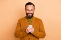 Photo of cheerful man hold telephone look screen wear eyeglasses brown cardigan isolated beige color background