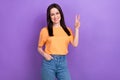 Photo of cheerful nice woman with straight hair dressed orange t-shirt showing v-sign arm in pocket isolated on purple Royalty Free Stock Photo