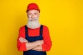 Photo of cheerful positive age man workwear overall red hard hat arms folded empty space isolated yellow color Royalty Free Stock Photo