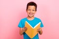 Photo of cheerful positive little boy dressed blue t-shirt reading interesting book isolated pink color background Royalty Free Stock Photo