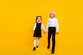 Photo of cheerful positive nice kids hold hands walk stroll wear school uniform isolated yellow color background