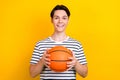 Photo of cheerful positive student with stylish hairdo dressed striped t-shirt hold bascketball ball isolated on yellow