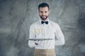 Photo of cheerful positive toothy beaming waiter holding tray with glasses of sparkling beverage isolated over grey