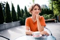 Photo of cheerful pretty girl dressed orange t-shirt sitting cafe enjoying morning coffee outdoors urban town park Royalty Free Stock Photo