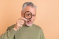 Photo of cheerful senior man watching through loupe ophthalmology check isolated over beige color background