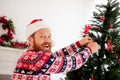 Photo of cheerful smiling man in santa hair decorating new year tree spruce celebrate merry christmas relaxing at home Royalty Free Stock Photo
