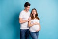Photo of cheerful sweet cute couple expecting child hugging belly looking each other isolated blue color background Royalty Free Stock Photo