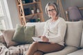 Photo of cheerful sweet elderly lady wear white cardigan sitting sofa writing notes copybook indoors apartment room