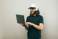 Photo of cheerful young bearded guy working on laptop and wearing white headphones Royalty Free Stock Photo