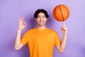 Photo of cheerful young positive man show okay sing spin basketball finger sport isolated on violet color background