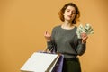Photo of cheerful young woman holding fan of money and colorful shopping bags, isolated on yellow background Royalty Free Stock Photo