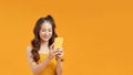 Photo of cheerful young woman standing isolated over yellow background. Looking aside using mobile phone Royalty Free Stock Photo