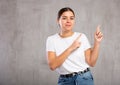 Cheery young woman pointing fingers away against gray background