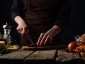 In the photo, a chef is slicing beets on a cutting board. In the photo in the right corner there are tomatoes. There is an empty