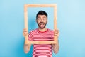 Photo of childish funny young guy wear red outfit holding looking wooden frame showing tongue isolated blue color