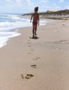 A photo with children`s footprints in the sand of the beach in the foreground and a little girl walking along the sea shore bac Royalty Free Stock Photo