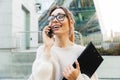 Photo closeup of beautiful smiling woman talking on cellphone and holding clipboard while walking in big city street Royalty Free Stock Photo